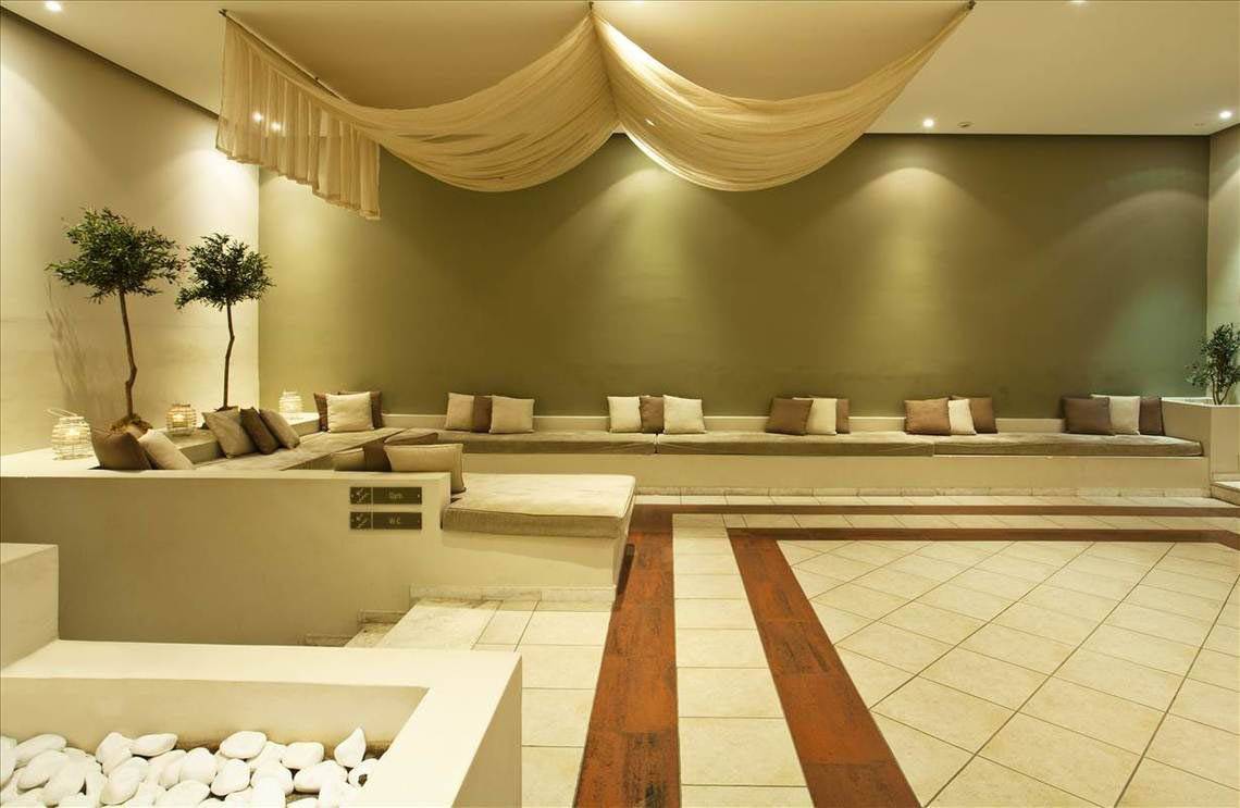 Loungebereich im Kipriotis Hippocrates Hotel mit Sofas, Pflanzen und Fliesenboden.