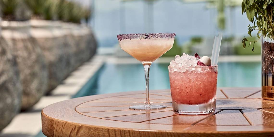 Zwei Cocktails auf einem runden Tisch neben einem Pool im Myconian Naia Hotel.
