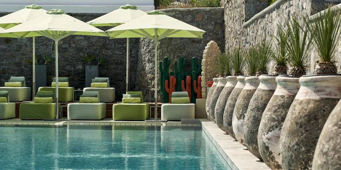 Poolbereich mit Loungemöbeln und großen grünen Sonnenschirmen im Myconian Naia Hotel.
