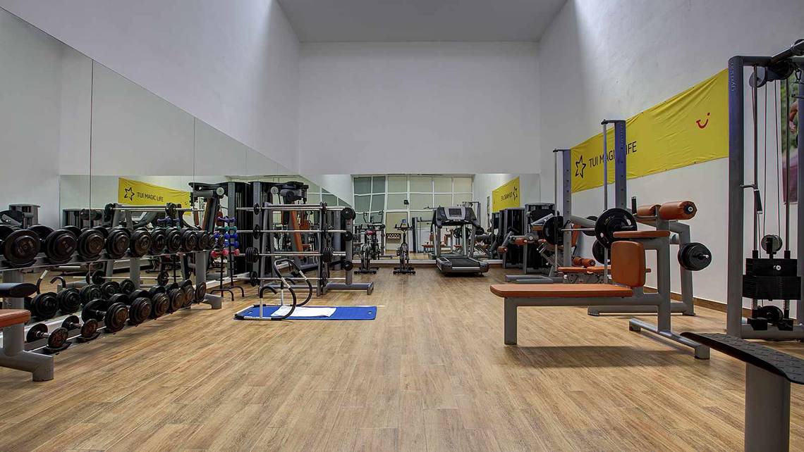 Fitness-Center im Atlantica Marmari Palace Hotel mit verschiedenen Trainingsgeräten und einer hölzernen Fitnessfläche.