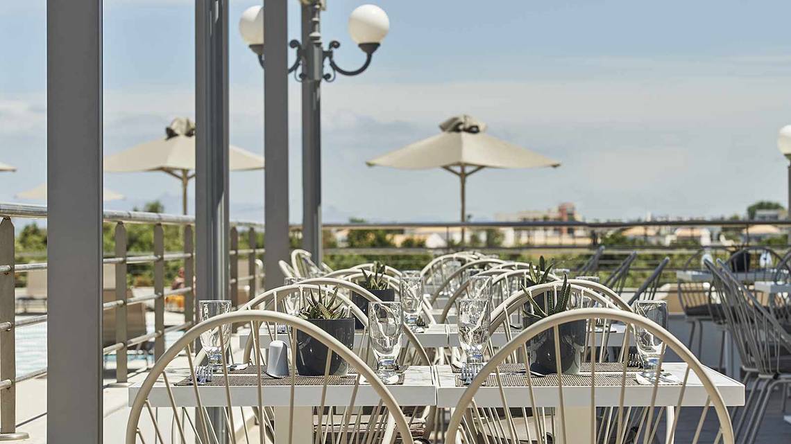 Dachterrasse des Atlantica Marmari Palace mit gedeckten Tischen und Sonnenschirmen.