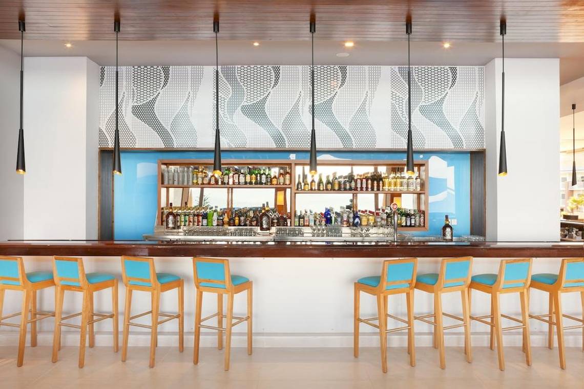 Innenansicht der Bar im Playa Vista Azul Hotel in Varadero mit blauen Stühlen und einer Bartheke voller Flaschen.