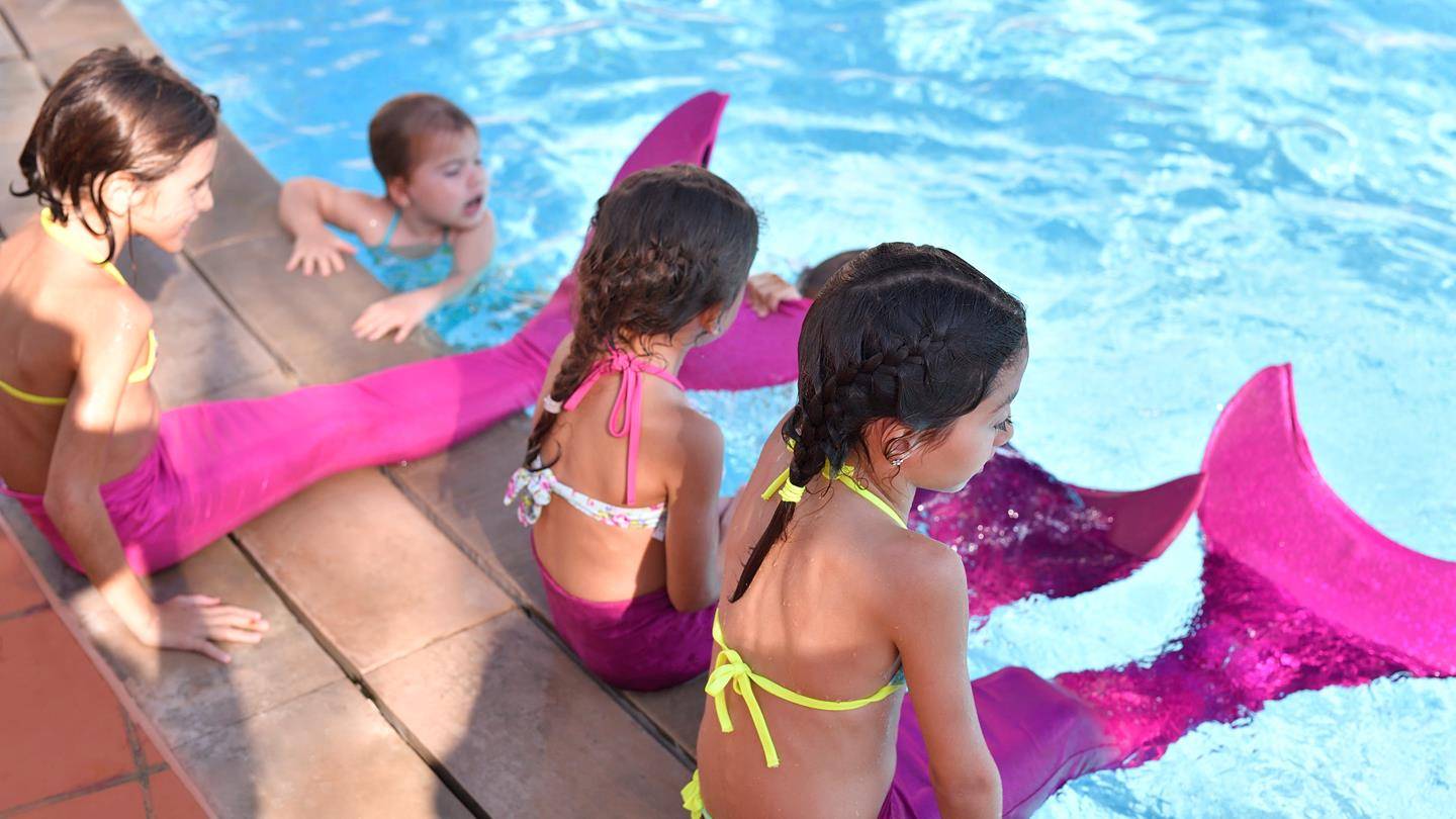 Kinder im Schwimmbad mit Mermaid-Schwänzen, eines schwimmt im Wasser