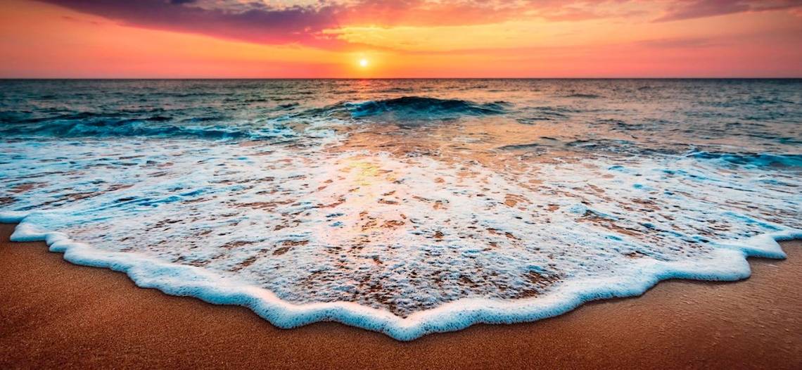 Sonnenuntergang am Strand, sanfte Wellen treffen auf den Sand, Fuerteventura Princess Hotel im Hintergrund.