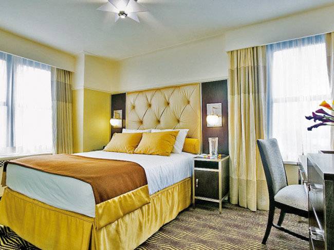 Schlafzimmer im The New Yorker Hotel mit einem großen Bett, gelben Kissen und einer modernen Einrichtung.