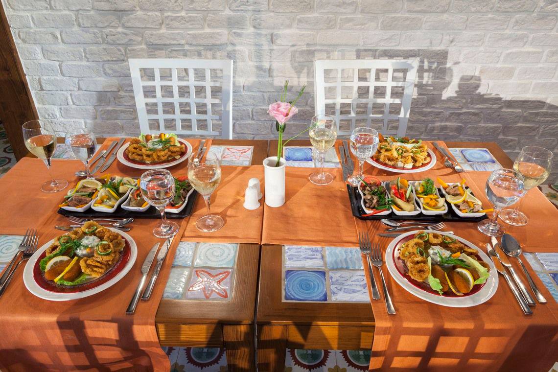 Ein Tisch mit mehreren Tellern Essen und Gläsern mit Getränken, darunter Wein, dekoriert mit einer Blume und serviert mit Besteck.