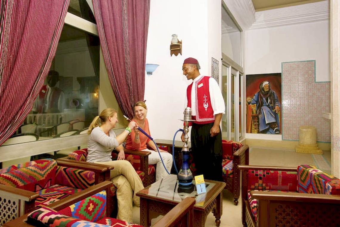 Im Hotel Calimera Yati Beach sitzen zwei Frauen in der Lounge und genießen eine Shisha, während ein Mann ihnen serviert.