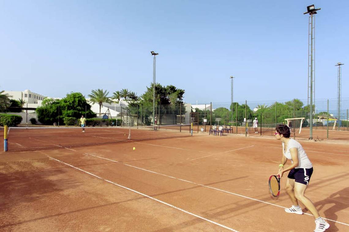 Tennisplatz im Calimera Yati Beach Hotel mit Spielerin, die einen Ball schlägt.