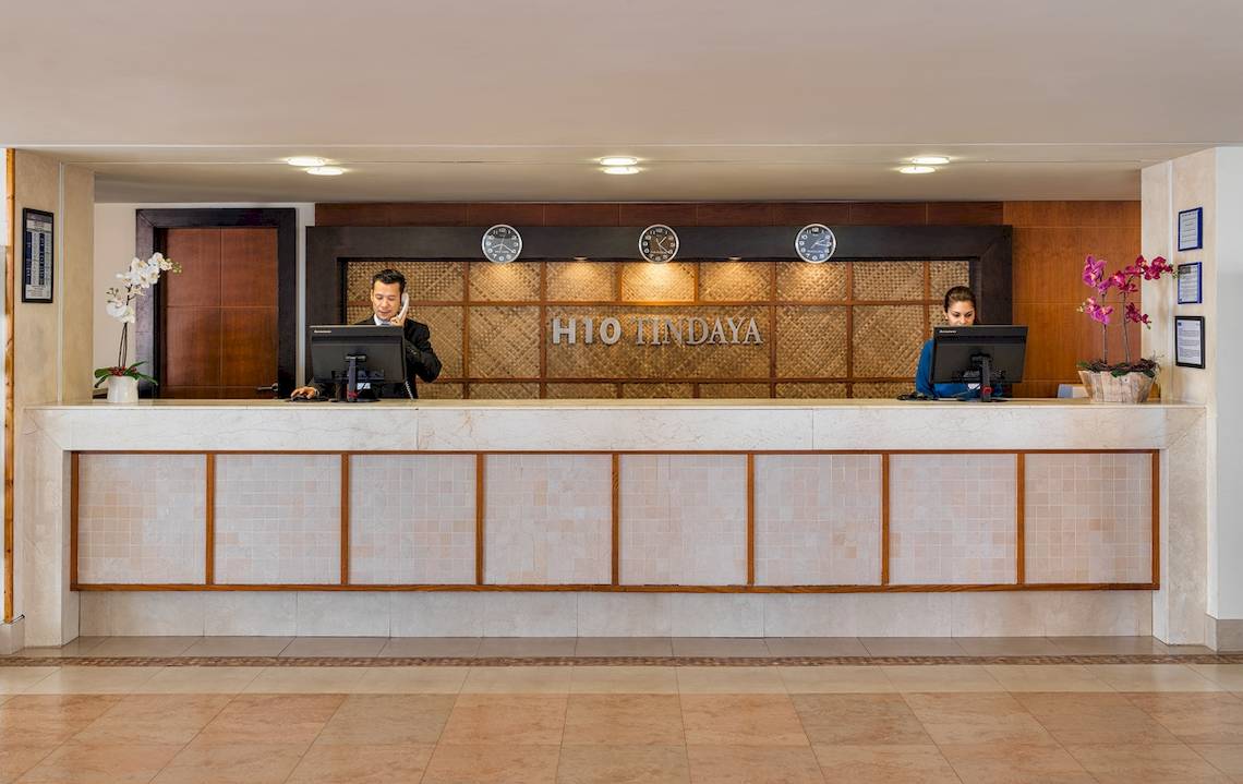 Die Rezeption des H10 Tindaya Hotels mit zwei Angestellten und dekorativen Pflanzen.
