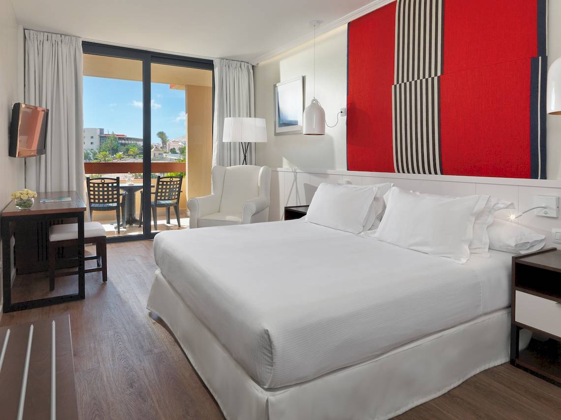 Hotelzimmer im H10 Tindaya mit Doppelbett, Sessel und Terrassenblick.