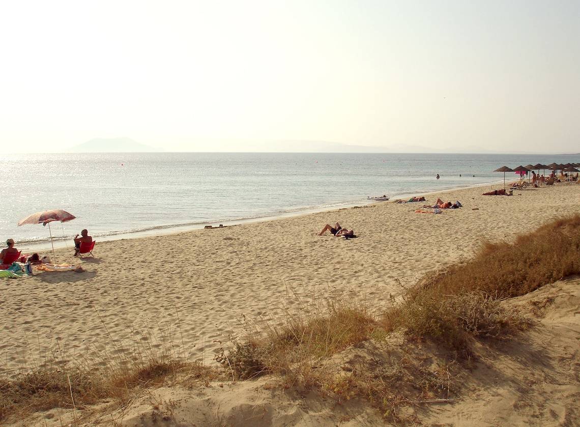 Leute, die am Strand sonnenbaden, mit Sonnenschirmen und Bergen im Hintergrund.