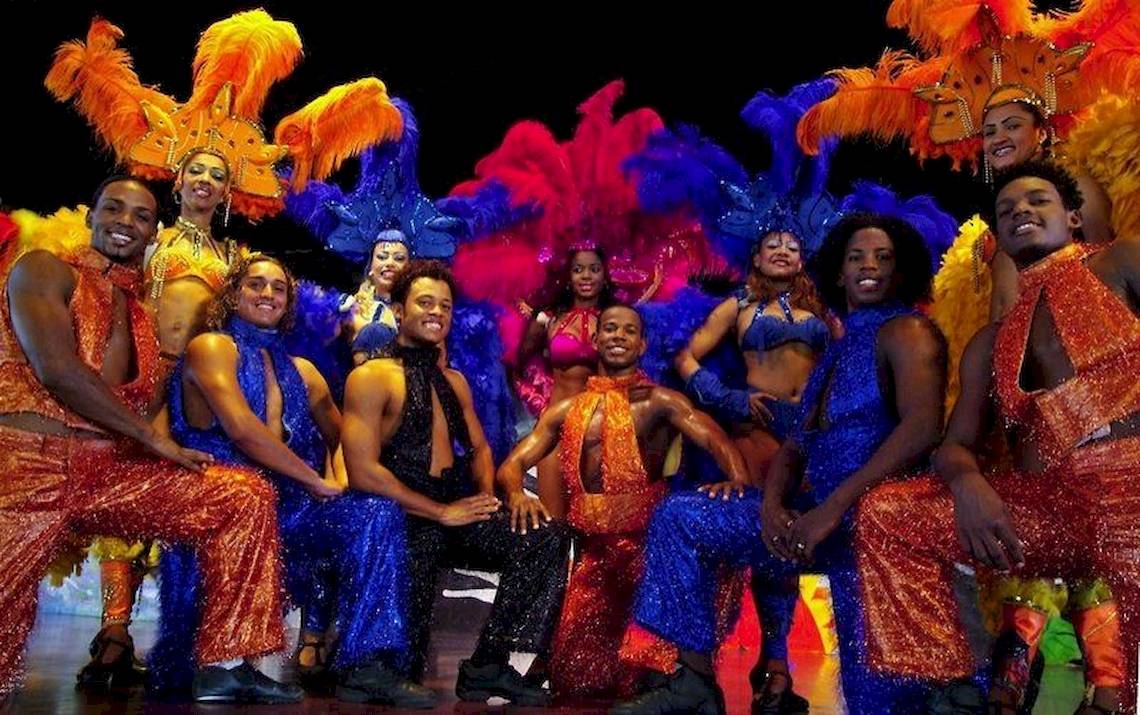 Gruppe von Performern in farbenfrohen Kostümen vor einer Bühne für eine Show im Bahia Principe Grand Bavaro Hotel.