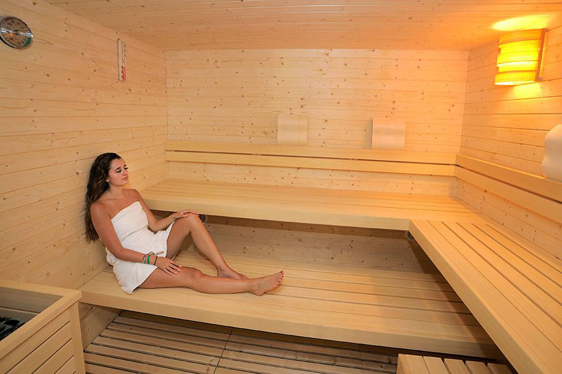 Eine Frau in einem weißen Handtuch sitzt in einer Holzsauna im Nelia Beach Hotel & Spa.