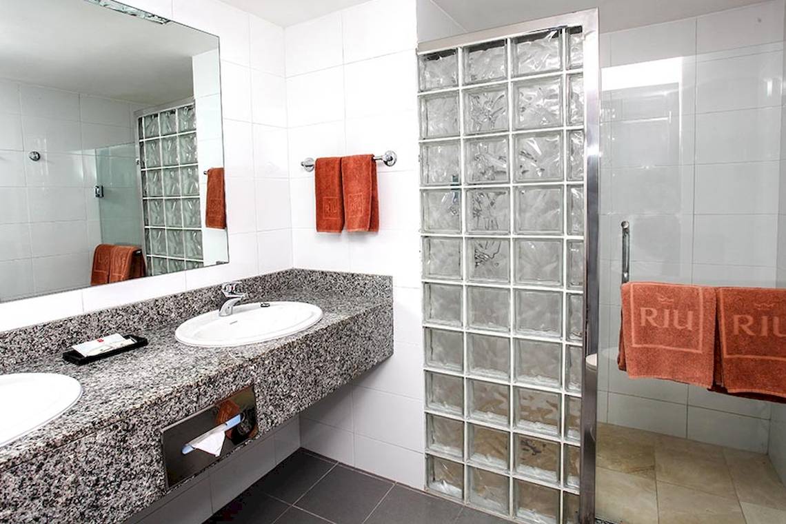 Badezimmer des Riu Naiboa Hotels mit zwei Waschbecken, Spiegel und Duschkabine.