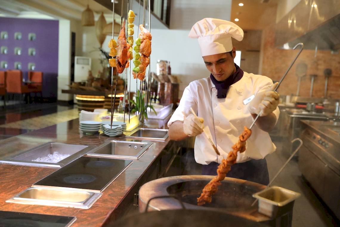 Ein Koch im Salinda Resort auf Phu Quoc Island bereitet Spießchen zu, während er in der Küche steht und einen Grillhaken hält.