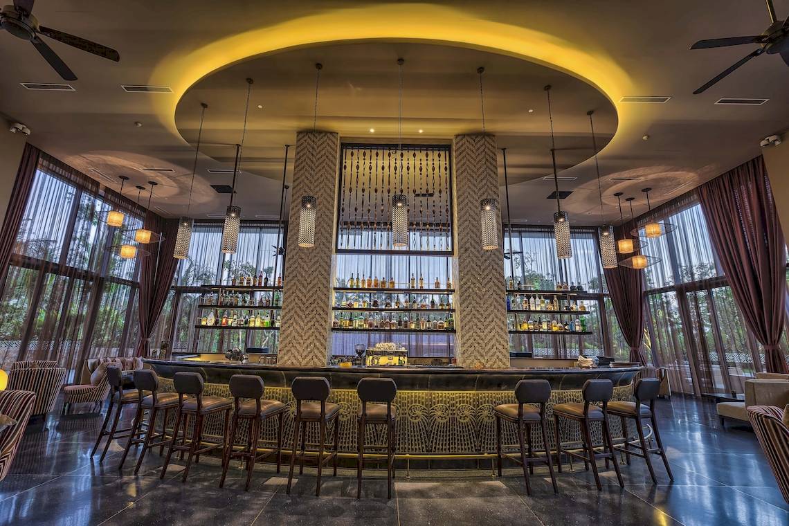 Innenansicht der Barlounge im Salinda Resort mit hohen Decken, hängenden Lampen und großen Fenstern.