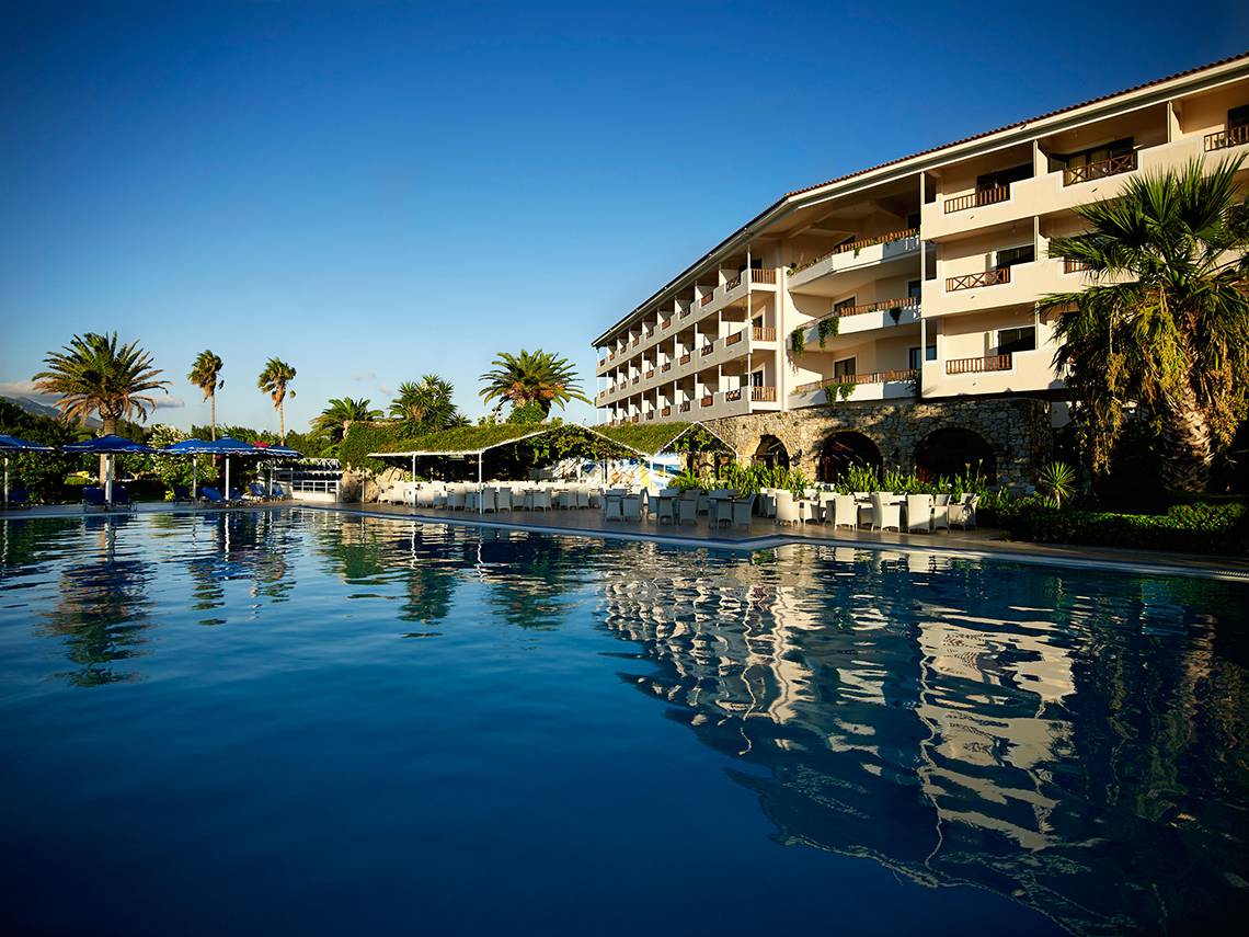 Außenpoolbereich des Mitsis Ramira Beach Hotels mit Sonnenschirmen und Liegestühlen.