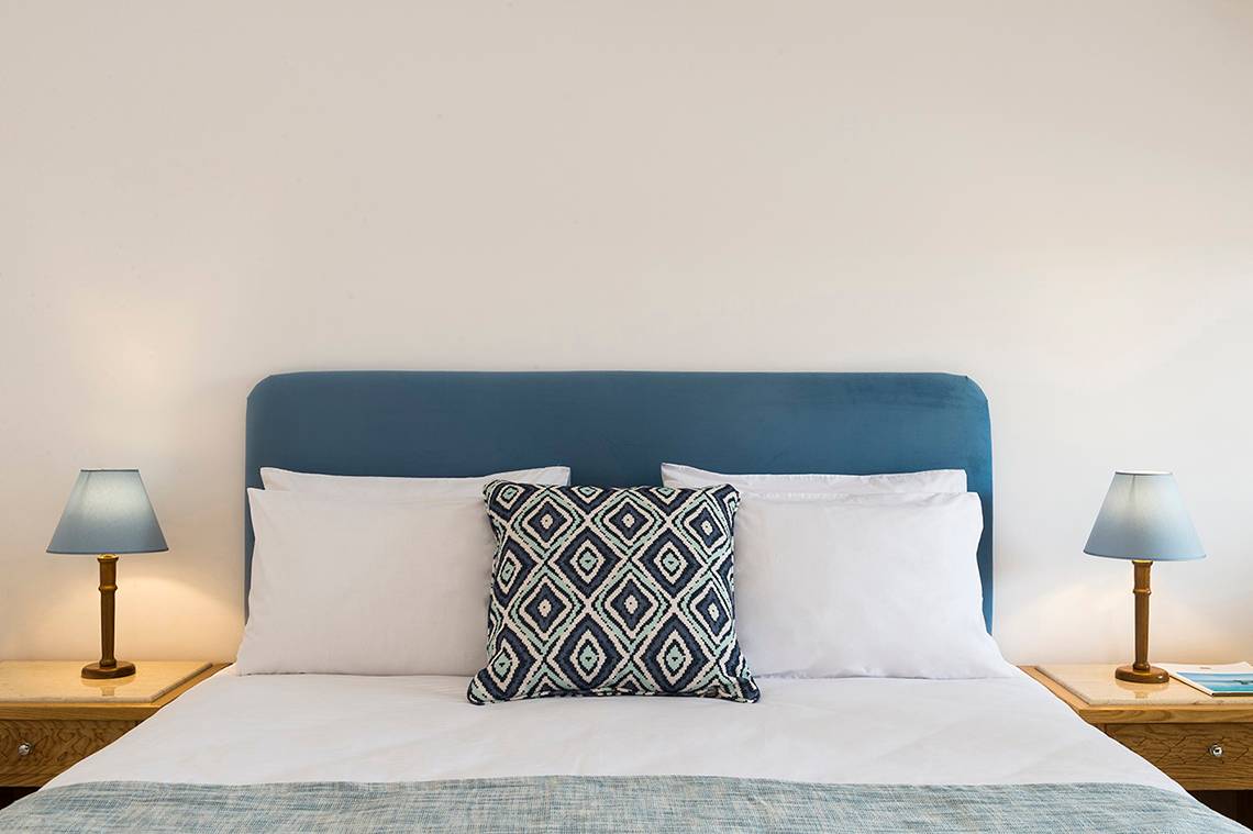 Ein Schlafzimmer im Mitsis Ramira Beach Hotel mit einem Bett, Kissen und Lampen auf den Nachttischen.