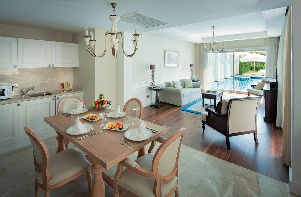 Suite-Esszimmer im Titanic Deluxe Golf Belek mit Esstisch, Früchteteller und Swimmingpool im Hintergrund.