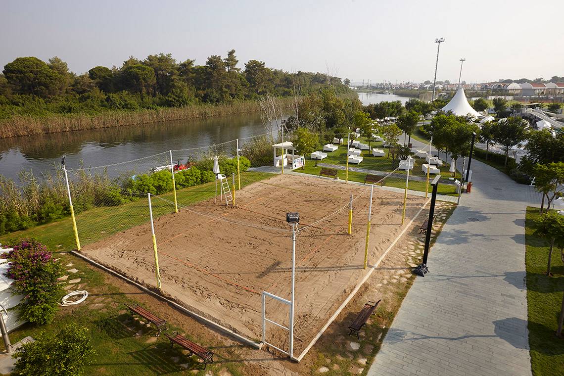 Luftaufnahme des Volleyballplatzes am Titanic Deluxe Golf Belek Hotel mit umliegendem Rasen und Bäumen.