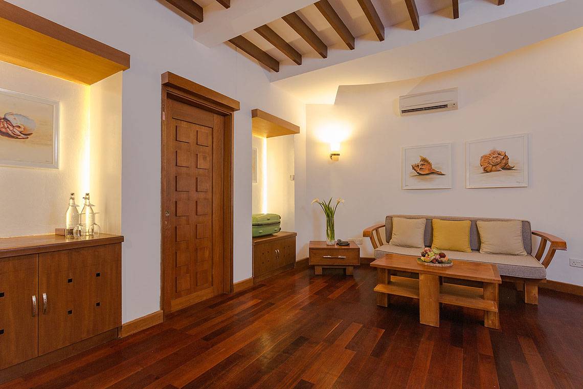Wohnbereich im Bandos Maldives Hotel mit Holzboden, Sofa, Couchtisch und Kunstwerken an der Wand.
