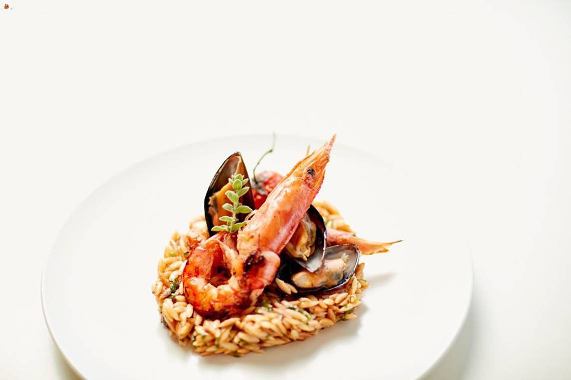 Ein Gericht mit Garnelen, Muscheln und Risotto auf einem weißen Teller.
