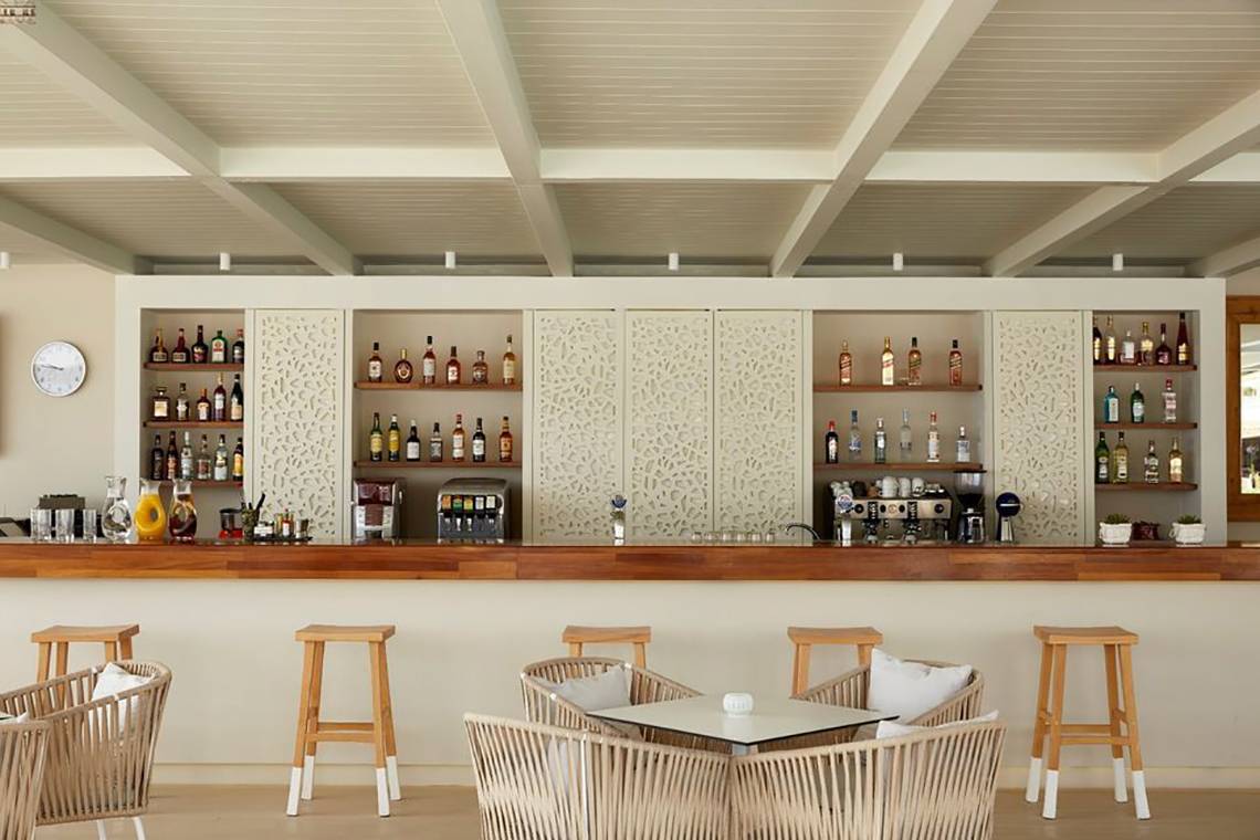 Innenansicht der Bar im Capo Di Corfu Hotel mit gepolsterten Stühlen und einer Theke voller Flaschen.