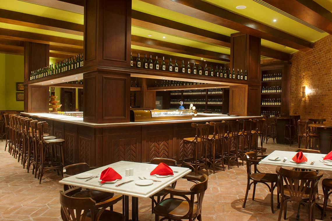Innenansicht der Bar im Makadi Spa Hotel mit Holztischen, Stühlen und einer Theke voller Flaschen.