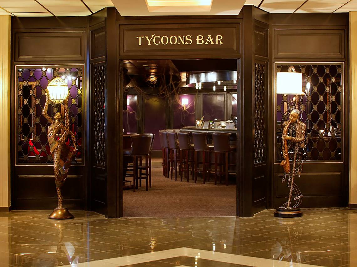 Eingang des Tycoons Bar im GrandResort Limassol mit zwei Statuen und einer offenen Tür.