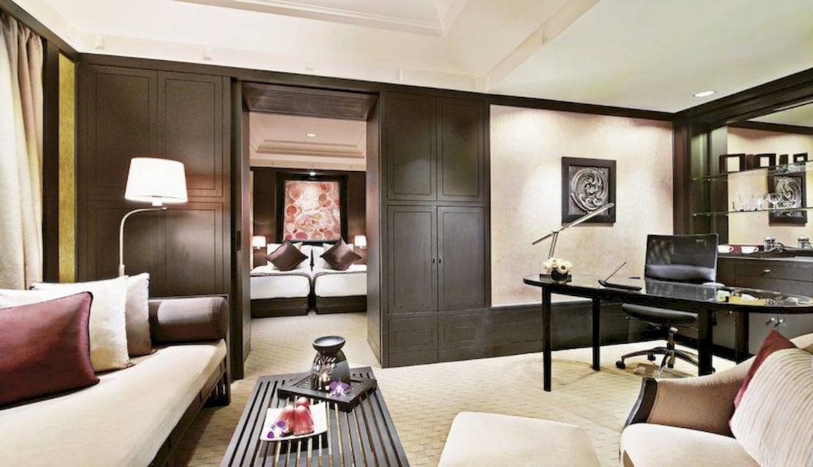 Innenansicht der Suite im Banyan Tree Bangkok mit Wohnzimmer, Schreibtisch und Schlafzimmerbereich.