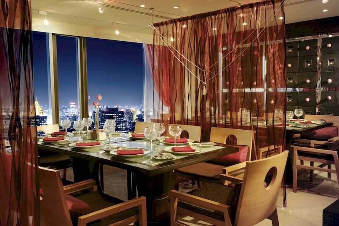 Innenansicht des Restaurants im Banyan Tree Bangkok mit Tisch, Stühlen und Aussicht auf die Stadt bei Nacht.
