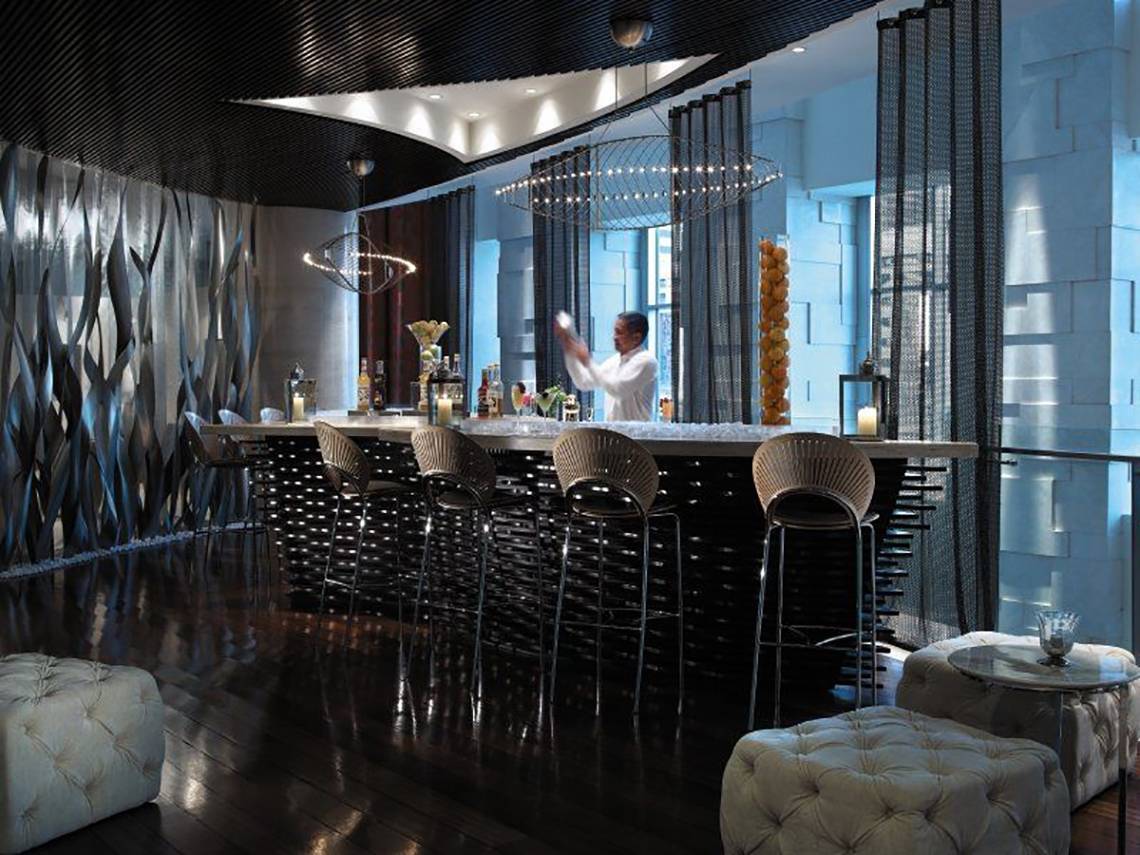 Hotellounge-Bar mit Barkeeper, der einen Cocktail mixt, während Gäste an der Bar sitzen.