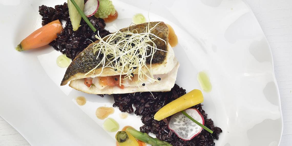 Gegrillter Fisch auf schwarzem Reis und Gemüse auf einem weißen Teller