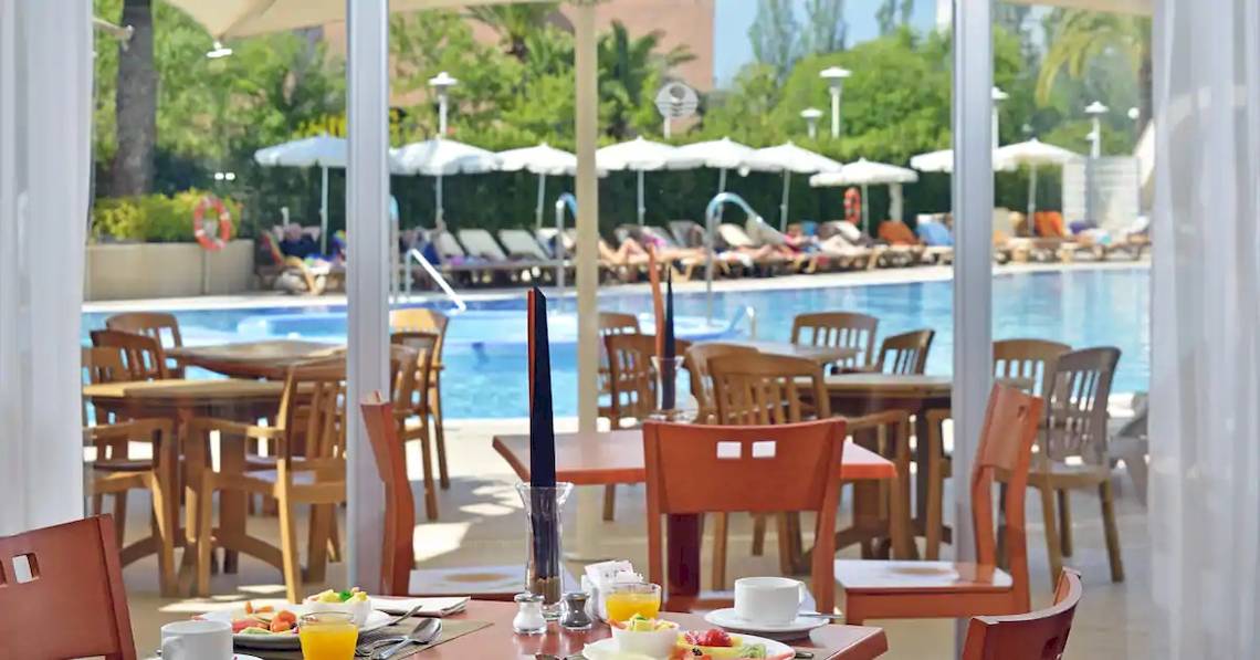 Poolseite des Sol Guadalupe Hotels mit Restaurant, Tischen, Stühlen und Sonnenschirmen.
