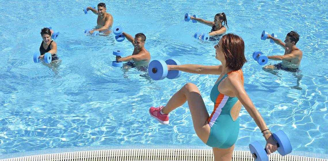Gruppe von Personen, die Aquafitness im Schwimmbad trainieren, mit Hanteln in der Hand.