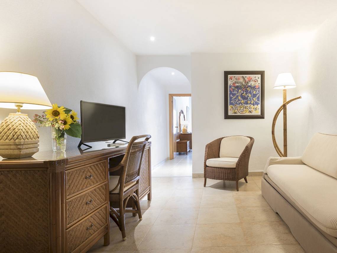 Innenansicht eines Zimmers im Princess Inspire Tenerife Hotel mit Schreibtisch, Sessel, Couch und Kunstwerk.