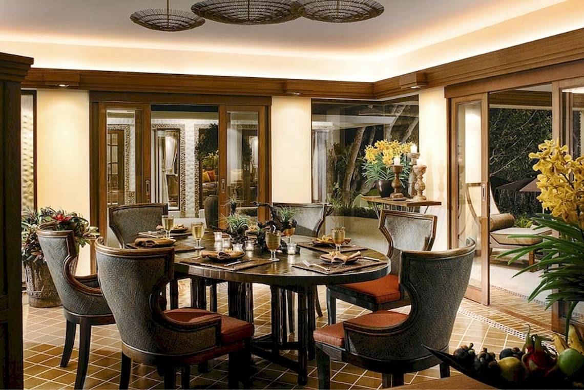 Esszimmer im Rayavadee Hotel mit runden Tisch und Stühlen, Glastüren und gelben Blumen im Vordergrund.