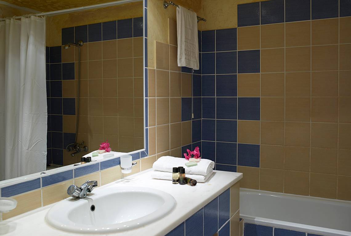 Badezimmer im Mitsis Summer Palace Beach Hotel mit blauen und braunen Fliesen und einem weißen Waschbecken.