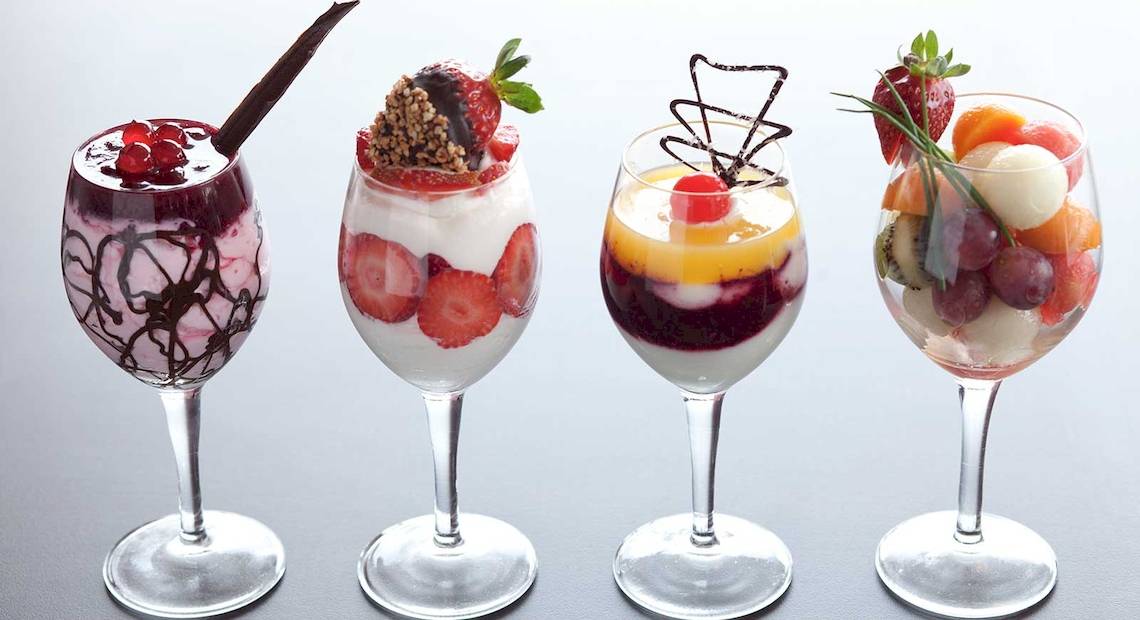 Vier fruchtige Cocktails in Gläsern mit Dekorationen wie Früchten und Schokoröllchen.