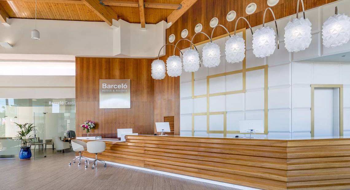 Empfangsbereich des Barcelo Fuerteventura Castillo Hotels mit Holzwand, Blumenvase und moderner Inneneinrichtung.