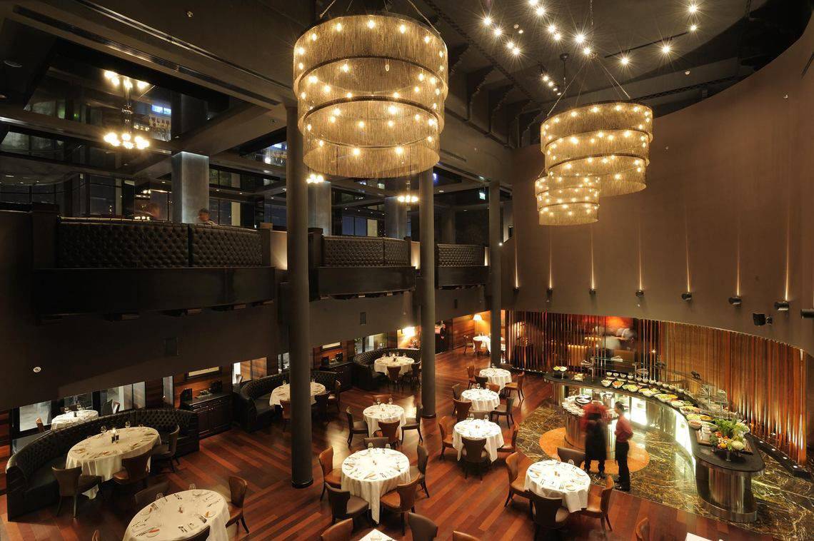 Innenbereich des Intercontinental Abu Dhabi Hotels mit mehreren Stockwerken, großen Kronleuchtern und gedeckten Tischen.