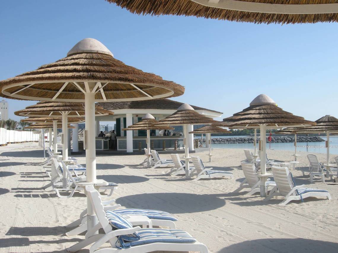 Strandszene mit weißen Sonnenliegen und Strohschirmen im Intercontinental Abu Dhabi