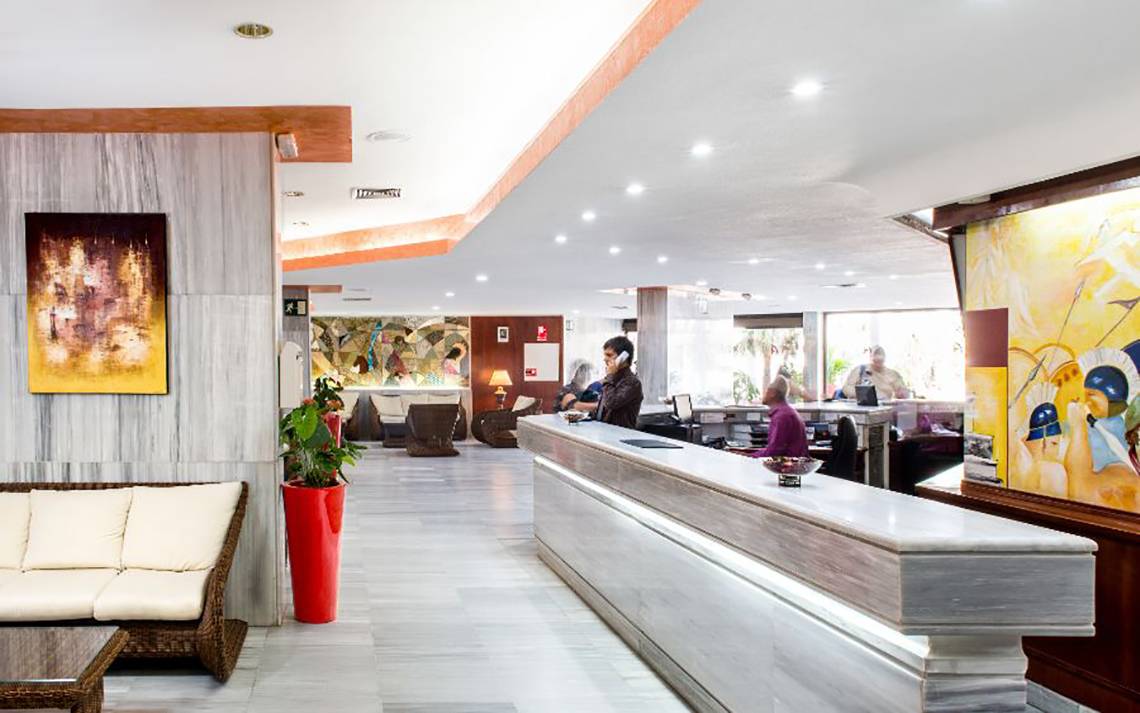 Empfangsbereich des Alexandre Hotel Troya mit Rezeption, Couch und Kunstwerken.