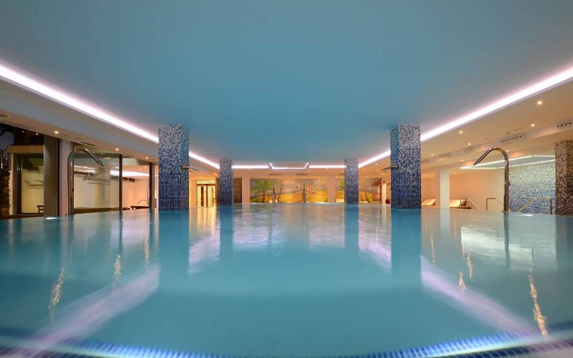 Innenpool des Alexandre Hotel Troya mit blauen Wänden und beleuchteten Säulen.