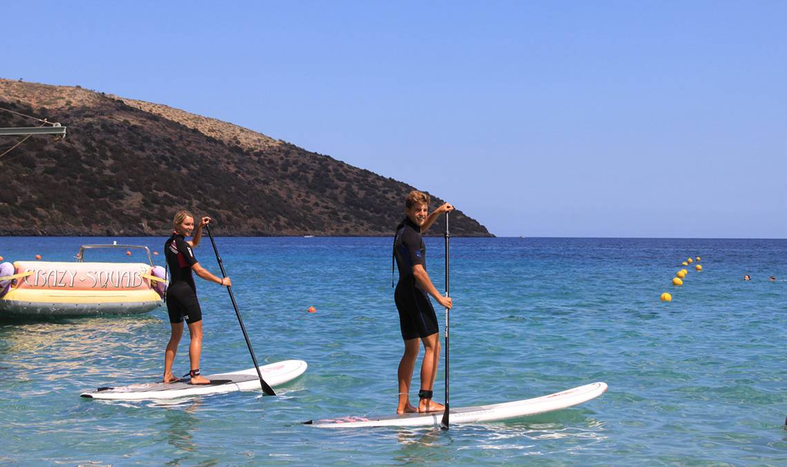 Zwei Personen auf SUP-Brettern im blauen Wasser mit einem Boot namens Crazy-Squad im Hintergrund.