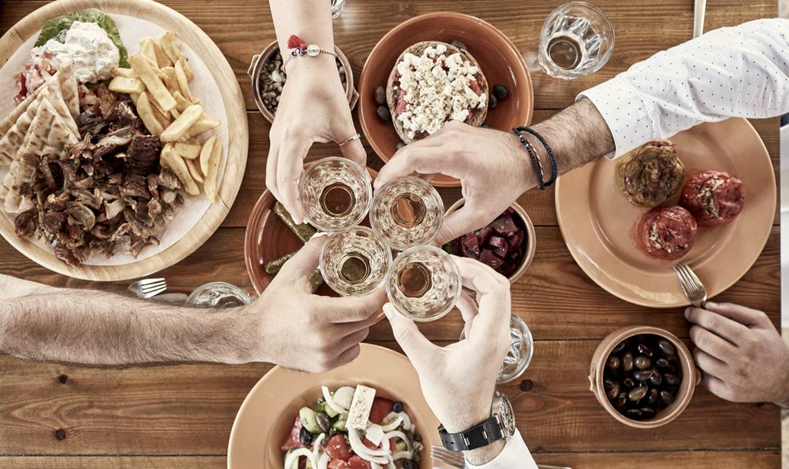Menschen am Tisch mit griechischem Essen, Salate, Fleisch und Getränke.