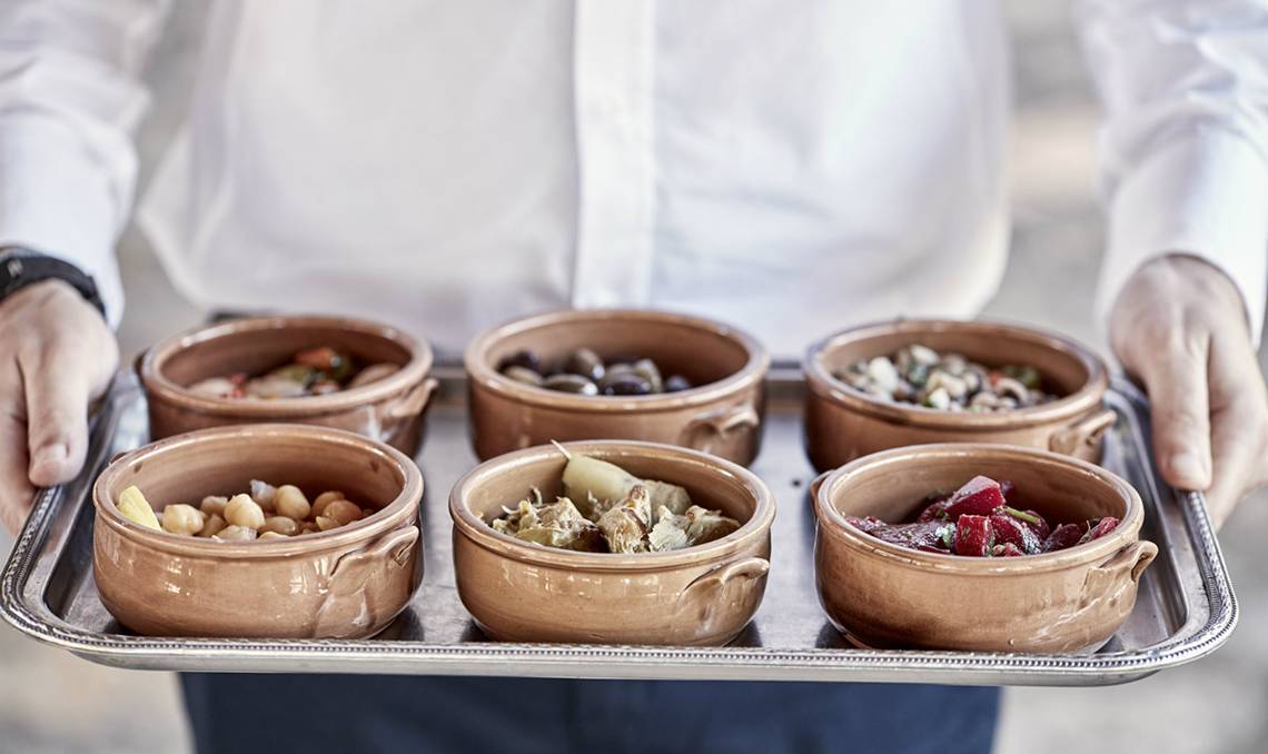 Servierteller mit kleinen Schalen gefüllt mit verschiedenen Vorspeisen wie Oliven, Bohnen und Artischocken.