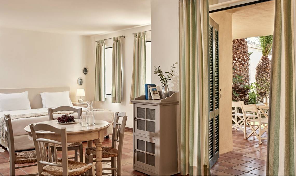 Innenansicht eines Zimmers im Candia Park Village Hotel mit einem Bett, Tisch und einem offenen Balkon