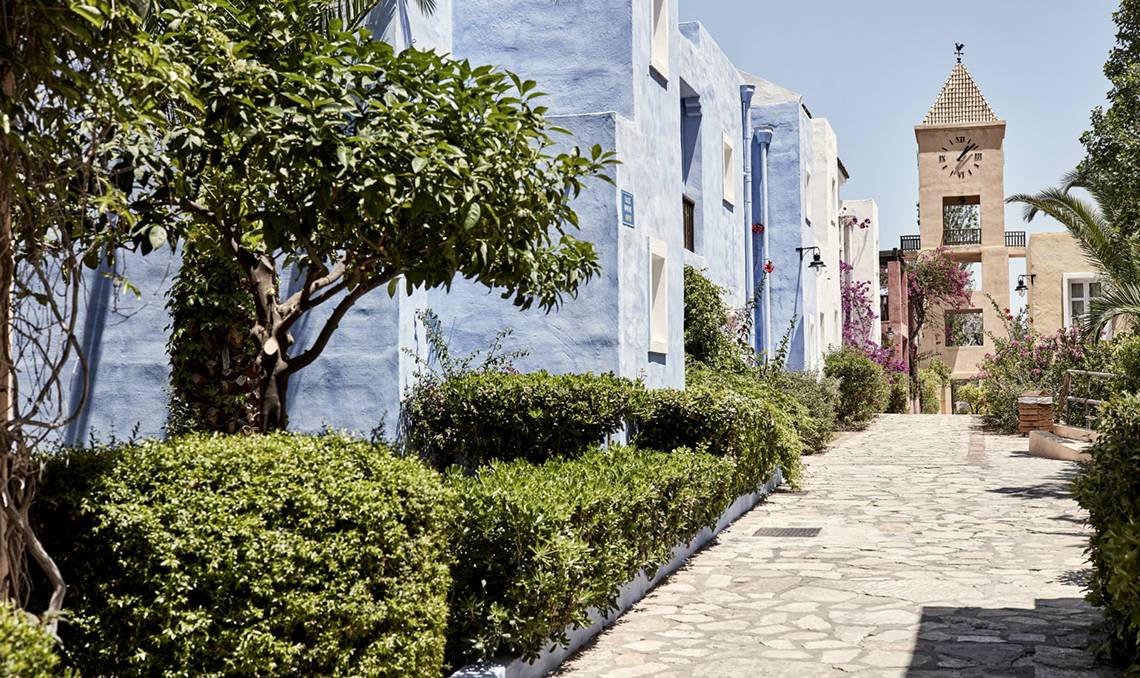 Candia Park Village Hotel Weg mit blauen Gebäuden und einem Turm im Hintergrund.