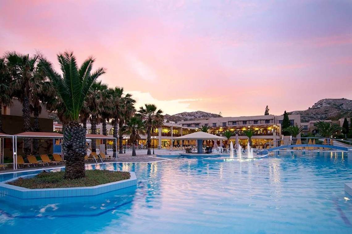 Außenbereich des Porto Bello Beach Hotels bei Sonnenuntergang mit Swimmingpool, Palmen und Blick auf das Gebäude.